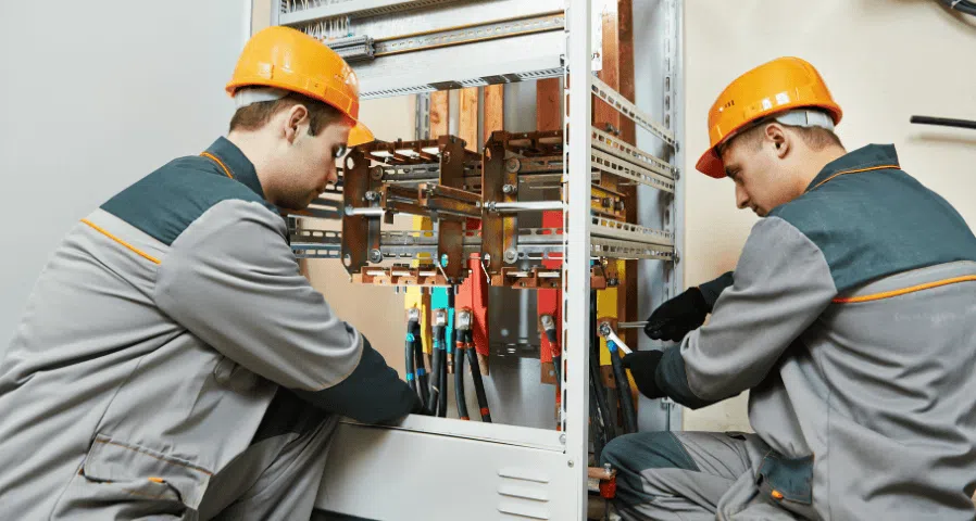 Two electricians in hard hats terminating heavy feeder cables at a switchgear cabinet with copper busbars — electrical contractor insurance in Minnesota