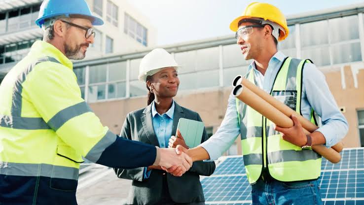Three people in hard hats and high-visibility vests shaking hands at a solar installation site — electrical contractor insurance in Mississippi