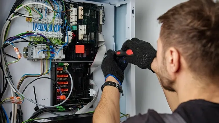 An electrician in gloves using a screwdriver inside a control enclosure of terminal blocks and relays — electrical contractor insurance in Washington