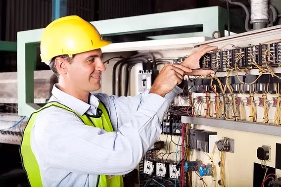 A smiling electrician in a hard hat and high-visibility vest working on an industrial machine control panel — electrical contractor insurance in Missouri