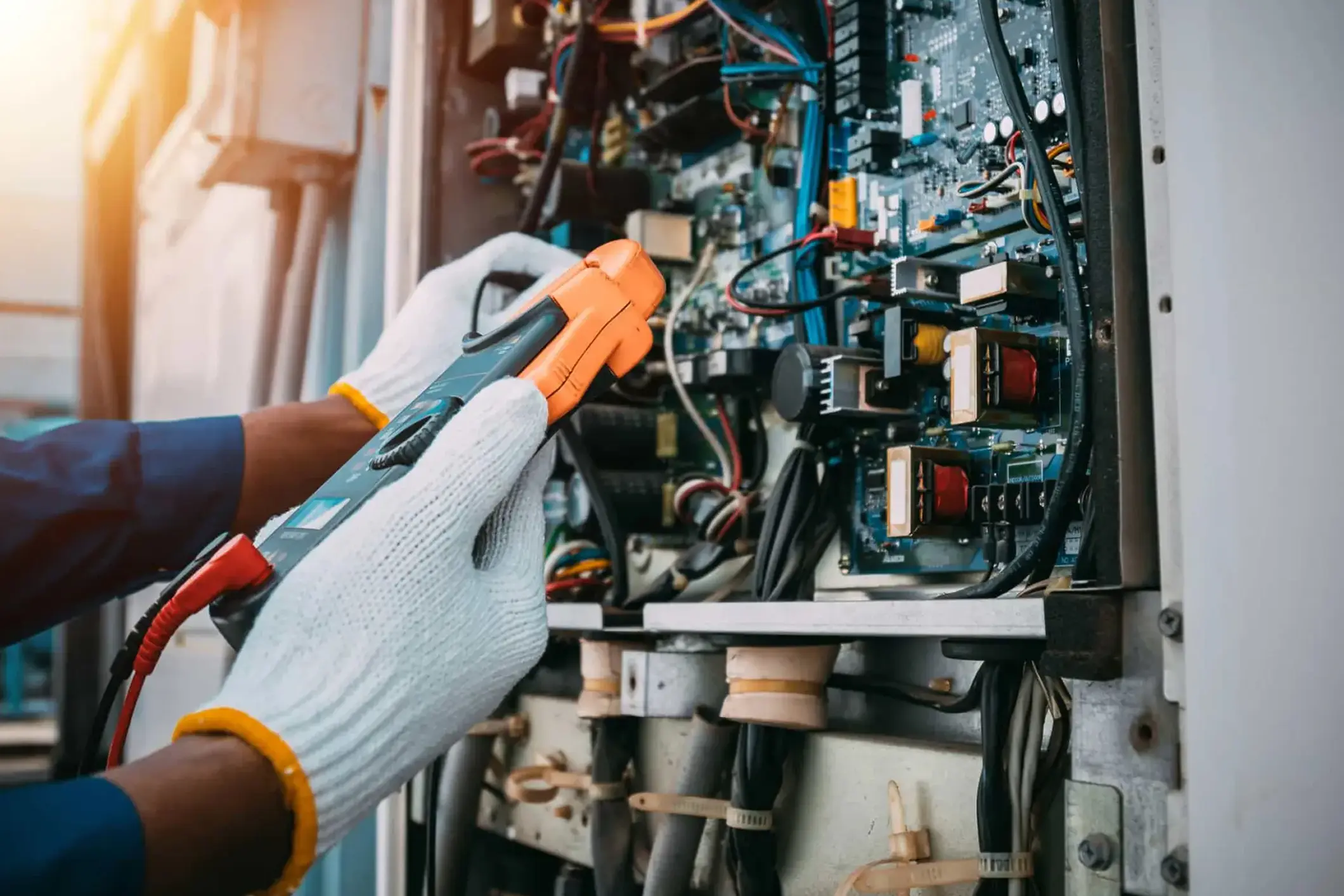 Gloved hands using a clamp meter to test a densely populated electronic control board — electrical contractor insurance in Connecticut