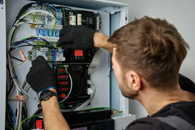 An electrician in gloves working inside a structured-wiring enclosure of terminal blocks and data cabling — electrical contractor insurance in Kentucky
