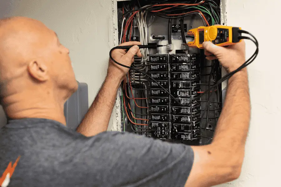 An electrician testing breakers in an open residential load center with a multimeter — electrical contractor insurance in Montana